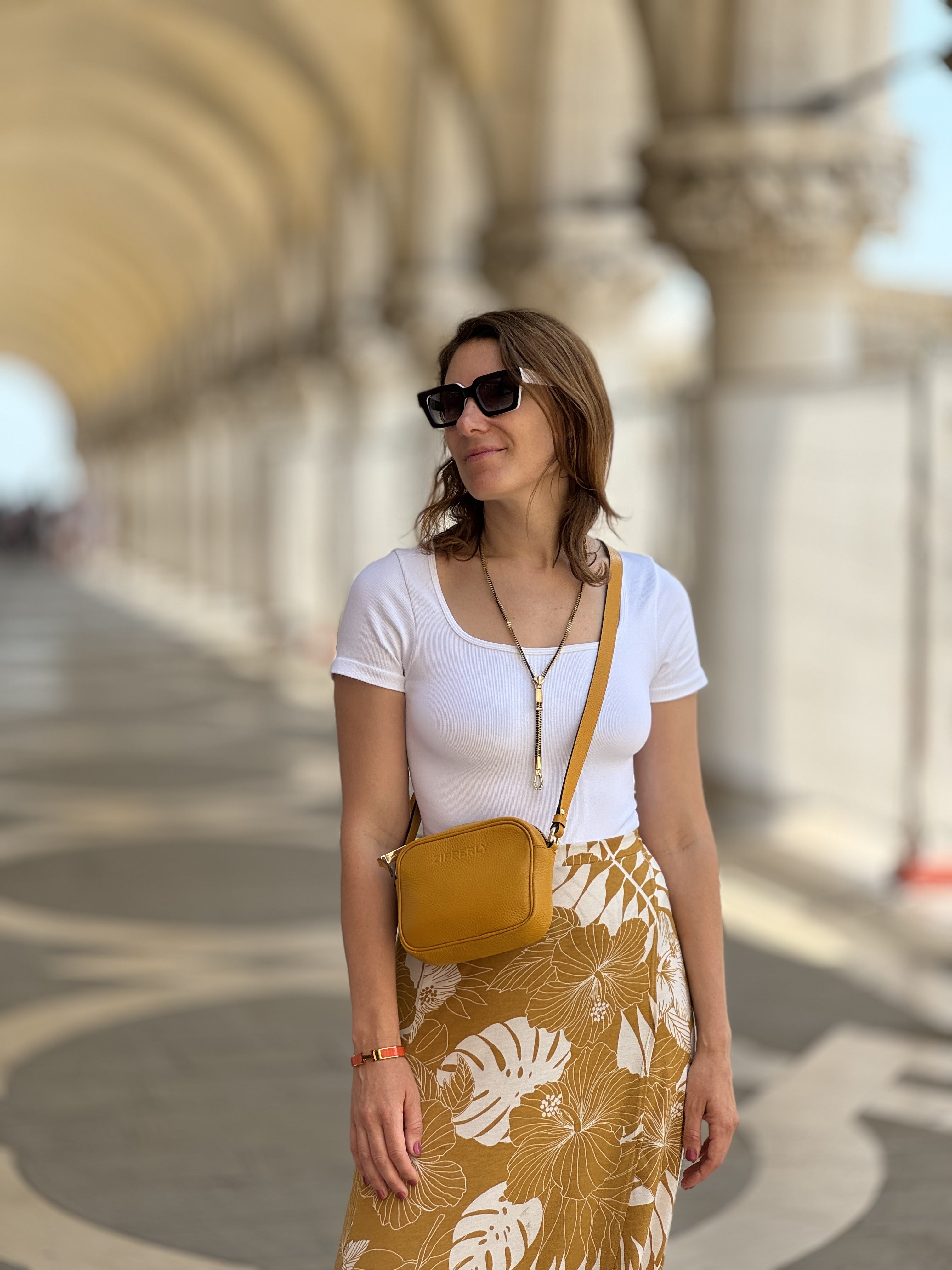 Woman in a white top and floral skirt with a yellow bag standing in an archway.