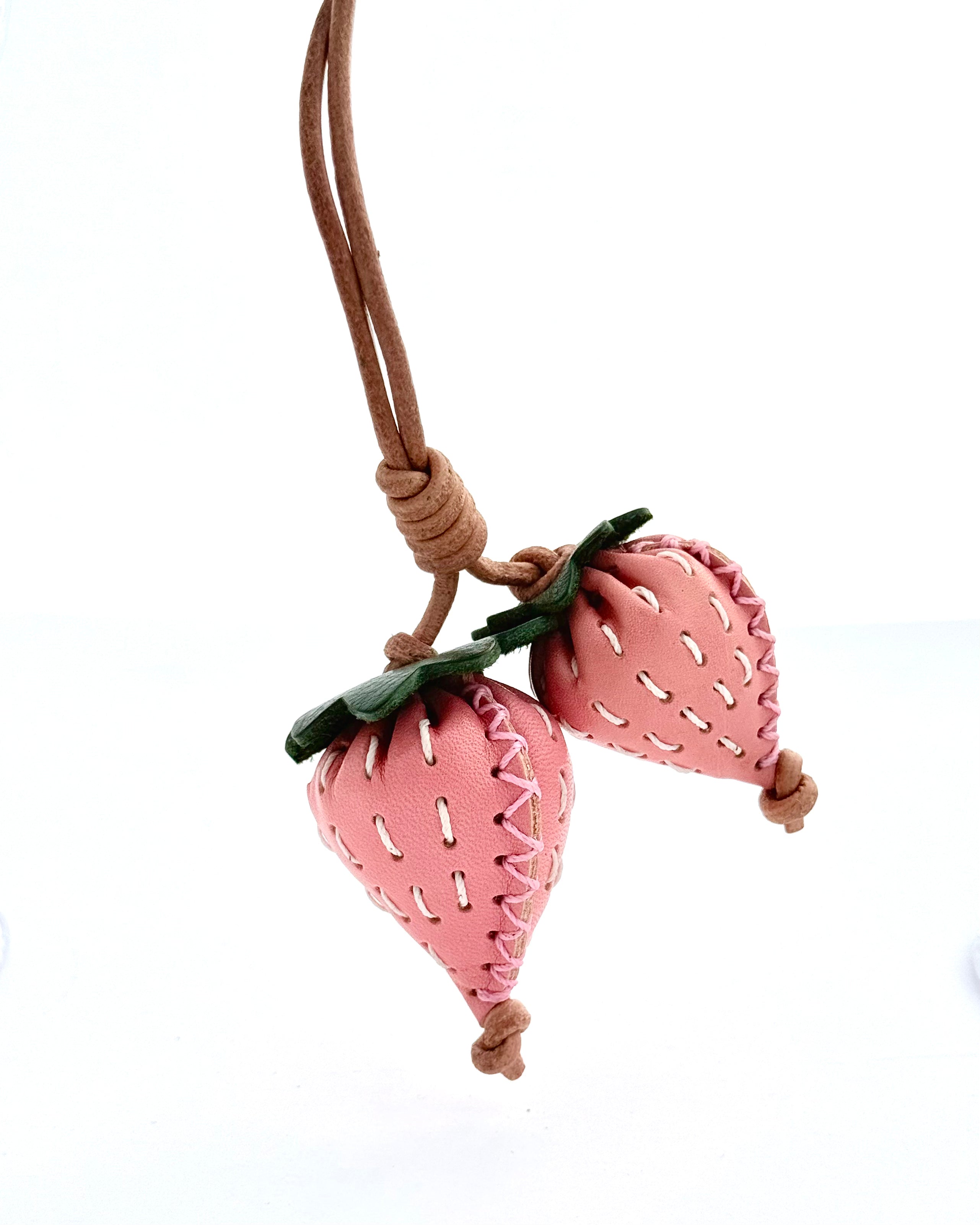 Pink strawberry-shaped bag charm, car charm or keychain on a brown cord against a white background