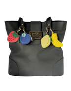 Black Zipperly Zoey Tote handbag featuring leather fruit bag charms — strawberry, blueberry, lemon, and banana — shown on a white background.
